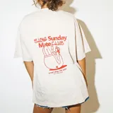 Remera color beige de algodón con estampa roja en la espalda que incluye una ilustración de una persona tomando mate y el texto "Slow Sunday Mate Club - Start your day right".