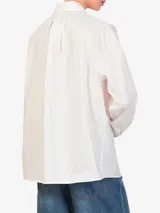 Camisa blanca de algodón con cuello clásico, manga larga con puños abotonados, cierre frontal con botones y bolsillo en el pecho. Incluye un bolo tie con cordón de cuero marrón y dije turquesa.