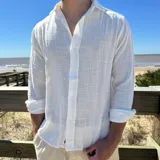 Camisa de manga larga color blanco, con textura de lino arrugado, cuello camisero y botones frontales.