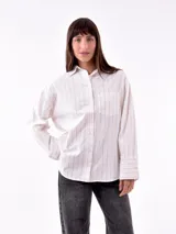 Camisa blanca con rayas verticales negras, de corte holgado, manga larga con puños abotonados y bolsillo en el pecho.