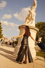 Vestido negro de cuero con tirantes anchos y escote recto. Presenta un detalle de costura decorativa con cordón azul oscuro a la altura de la cintura.