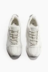 Championes deportivos blancos con detalles en gris, confeccionados en malla y tejido revestido, con cierre de cordones y suela gruesa con diseño.