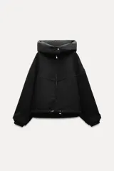 Chaqueta negra de cuello redondo confeccionada en hilatura con 50% lana. Tiene capucha extraíble, manga larga con puño interior, bolsillos delanteros y bajo ajustable con cordón elástico. Cierre frontal con cremallera metálica.