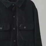 Campera negra de pana con cuello camisero, cierre frontal con botones a presión, dos bolsillos de parche en el pecho y corte recto.