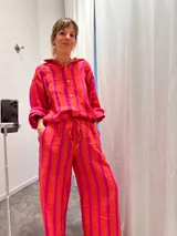 Conjunto de camisa y pantalón de tela arrugada con rayas verticales rosas y naranjas. La camisa es de manga larga con cuello y cierre frontal con botones. El pantalón es de corte ancho con cintura elastizada y cordón ajustable.