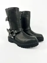 Bota negra de cuero con caña media, suela track, correa con hebilla en el tobillo y arnés con argolla metálica.