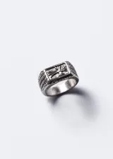 Anillo signet rectangular de acero quirúrgico pulido, con cruz estilizada en alto relieve y grabados geométricos en los laterales.