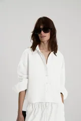 Camisa crop de lino y algodón color blanco, con cuello camisero y aberturas en la espalda, mangas largas con puños con tablas.