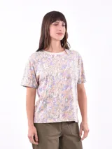 Remera estampada con flores en tonos lila, naranja y verde sobre fondo blanco.