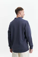 Sweater verde oliva de punto con cuello alto y cierre de medio cierre. Tiene puños y logo bordado en el pecho.