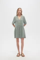 Vestido corto color crema, de corte holgado, con cuello en V y botones frontales.