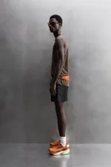 Pantalón corto deportivo color marrón oliva, con cintura elástica ajustable con cordón, bolsillos frontales y bolsillo trasero con cierre. Presenta forro interior y detalle de logo estampado en la pernera.