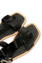 Sandalia plana negra de cuero con tira delantera y tira al tobillo con hebilla metálica plateada.