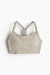 Top deportivo color beige de tejido acanalado con tecnología DryMove™ que absorbe el sudor. Tiene breteles finos, espalda nadadora, copas forradas con relleno extraíble y bajo elástico acanalado.