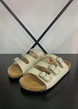 Sandalias beige con tres tiras horizontales ajustables con hebillas plateadas, plantilla de corcho y suela plana.