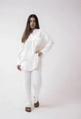 Camisa blanca de lino, de corte holgado, con cuello clásico, cierre frontal con botones, bolsillo en el pecho y mangas largas con puños abotonados.