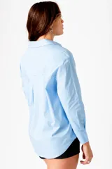Camisa celeste de corte clásico, con cuello camisero, manga larga y cierre frontal con botones.
