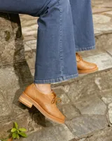 Zapato acordonado color bronce de cuero vacuno con perforaciones decorativas, taco de madera con folia en cuero de 4cm y entre suela de goma de 1,5cm. Horma de punta redonda y cómoda.