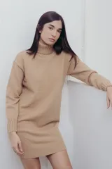 Vestido corto color beige de tejido de punto, con cuello alto tipo polera y mangas largas. Corte recto y terminaciones acanaladas en puños, cuello y ruedo.