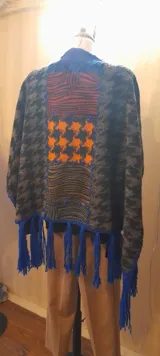 Ruana artesanal con diseño de patchwork en la espalda, terminación de pespuntes y crochet en lana con flecos azules.