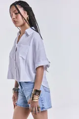 Camisa blanca de mangas cortas con dobladillo, cuello clásico, cierre frontal con botones y dos bolsillos frontales con solapa.