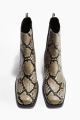 Botas Chelsea de mujer con estampado de piel de serpiente en tonos beige, negro y marrón. Presentan punta y taco cuadrados, elásticos laterales negros y una trabilla trasera para facilitar el calce.