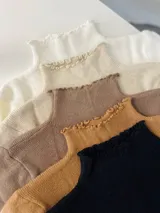 Polera de cuello alto con volados en el cuello, de tejido de punto fino en colores blanco, beige, marrón, mostaza y negro.