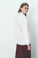 Camisa blanca oversize de popelina de algodón, con cuello solapa, manga larga con puños y cierre frontal con botones ocultos. Detalle de hilo de contraste en los botones.