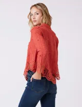 Camisa de algodón color naranja, con bordado suizo y encaje calado. Tiene cuello con solapa, botones frontales, mangas largas con terminación de encaje y ruedo asimétrico con galón de encaje.