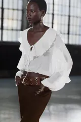 Blusa color marrón con escote en pico, manga larga abullonada con elástico en los puños y volantes en el escote y mangas.