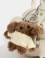 Cartera bandolera color crema con múltiples bolsillos frontales y laterales, doble asa corta regulable y charm de oso de peluche.