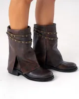 Bota corta de cuero color marrón con suela de goma negra, taco de madera de 3cm y caña de 25cm. Presenta una correa con hebilla y tachas pequeñas alrededor del tobillo.