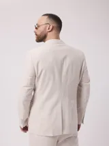 Saco de lino color beige con rayas verticales, solapa de muesca, cierre de dos botones, tres bolsillos frontales y puños con cuatro botones.