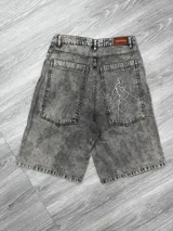 Bermuda de jean gris oscuro con efecto acid wash, corte ancho y tiro alto. Presenta un parche de cuero marrón con el texto "JAQUEMATE" en la parte trasera de la cintura y un rayo blanco pintado sobre el bolsillo trasero derecho.