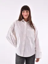 Camisa blanca con rayas verticales negras, de corte holgado, manga larga con puños abotonados y bolsillo en el pecho.