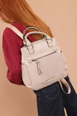 Mochila bandolera color marrón con herrajes color peltre. Tiene un compartimento principal amplio con cierre, un bolsillo frontal con cierre y dos bolsillos laterales abiertos. Incluye correa ajustable para usar al hombro o cruzada.