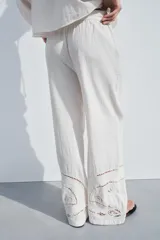 Pantalón de tiro medio color crudo, confeccionado en mezcla de algodón y lino, con cintura elástica ajustable con cordones, bolsillos laterales ocultos y detalle de bordados perforados a tono en el ruedo.