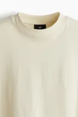 Remera color crema de algodón de peso medio, con cuello redondo ribeteado, hombros caídos, corte oversized y bajo recto.
