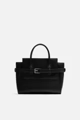 Bolso bandolera negro con detalle de cinturón, compartimento principal con cierre mediante doble imán, bolsillo interior con cierre mediante cremallera, dos asas de mano y un asa de hombro ajustable y extraíble.