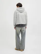 Buzo con capucha gris claro melange, de manga larga y corte relajado. Confeccionado en tejido loop back cepillado, con mangas ranglán, puños de canalé, bolsillo canguro y estampa en la espalda.