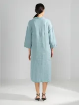 Camisa larga blanca de lino italiano, con cuello clásico, mangas 3/4, silueta fluida, dobladillo curvado en las costuras laterales y bolsillos discretos.