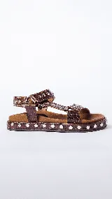 Sandalias marrones con textura de piel de cocodrilo, plataforma plana con tachas plateadas y tiras anchas con hebilla ajustable.