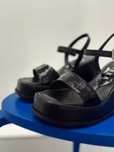 Sandalias negras de plataforma con tira ancha sobre el empeine y pulsera al tobillo con hebilla metálica.