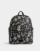 Mochila negra con estampado de margaritas blancas, confeccionada en cuero sintético. Cuenta con correas regulables, manija superior, acceso con cierre, bolsillo frontal con cierre y tag de cuerina. Incluye un pouch extraíble.