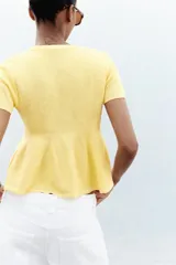 Chaqueta color amarillo claro de tejido de punto, con cuello redondo, manga corta, cierre frontal con botones y bajo evasé.