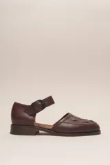 Zapato marrón de cuero vacuno con diseño trenzado en la parte delantera, tira sobre el empeine con hebilla y taco bajo. Hecho a mano en Argentina.