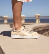Zapatillas acordonadas de cuero color marrón con detalles dorados en el talón y suela blanca.