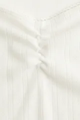 Remera corta blanca de punto suave con textura acanalada. Modelo ajustado con costura fruncida en el centro del busto y escote corazón pronunciado con ribete de picot.