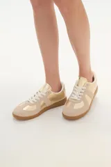 Zapatillas deportivas color beige y dorado con suela marrón.