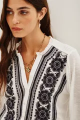 Camisa blanca de manga larga con cuello mao y escote en V, con bordados negros en el frente y puños.